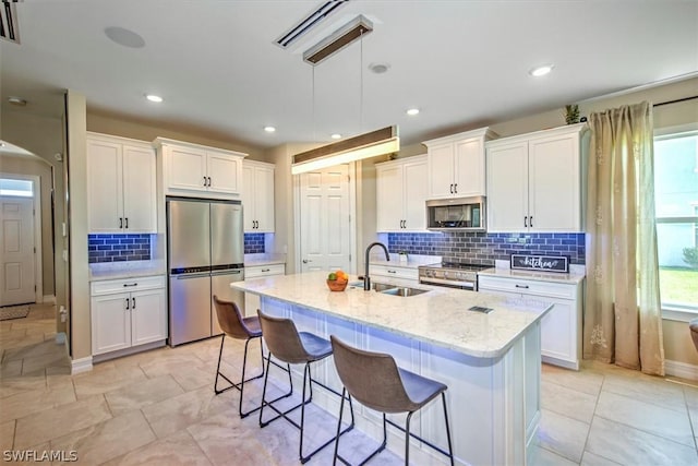 kitchen featuring light stone countertops, appliances with stainless steel finishes, a center island with sink, and white cabinetry