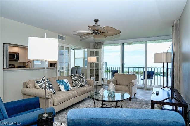 living room featuring wood-type flooring, a water view, sink, and ceiling fan