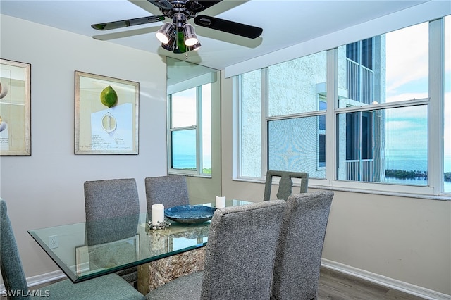 dining space with a water view, wood-type flooring, and ceiling fan