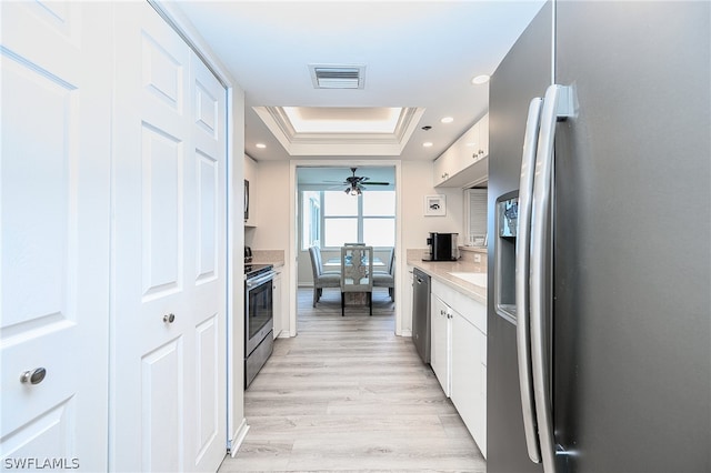 kitchen featuring white cabinetry, light hardwood / wood-style flooring, ceiling fan, appliances with stainless steel finishes, and a raised ceiling