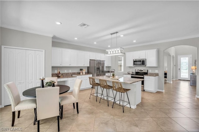 kitchen with a center island with sink, arched walkways, visible vents, stainless steel appliances, and a kitchen bar