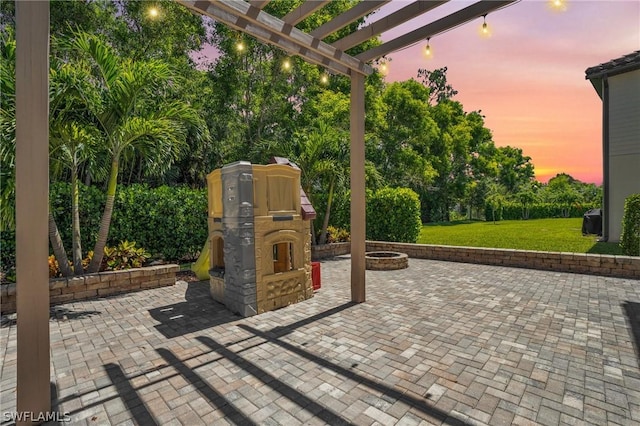 patio terrace at dusk featuring a yard, a fire pit, and a pergola