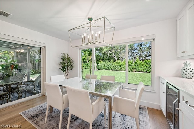 dining space featuring an inviting chandelier, light hardwood / wood-style flooring, and wine cooler