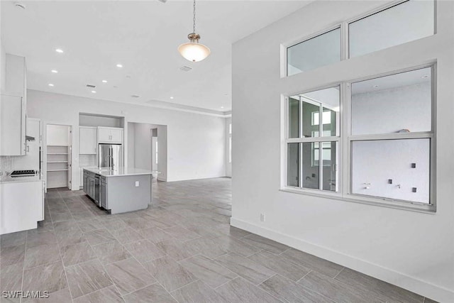 kitchen featuring pendant lighting, stainless steel refrigerator, an island with sink, and white cabinets