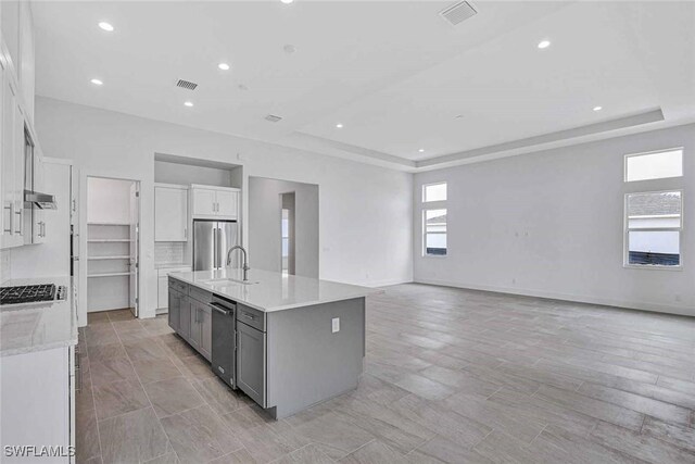 kitchen with sink, gray cabinets, a kitchen island with sink, high quality fridge, and a raised ceiling