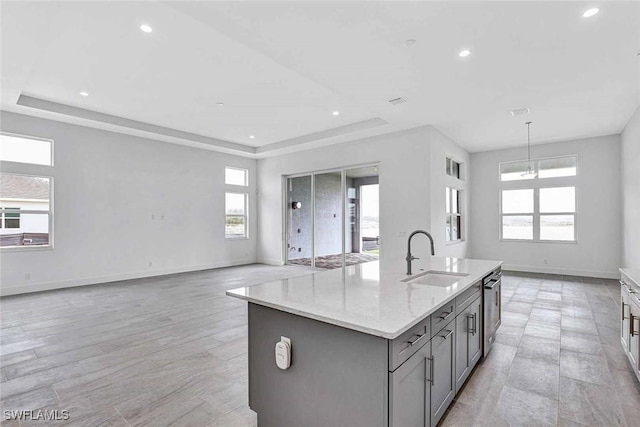 kitchen featuring a kitchen island with sink, a raised ceiling, sink, and light stone countertops