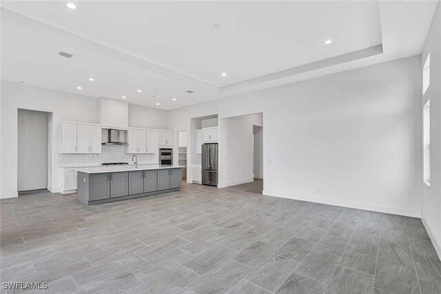 kitchen featuring white cabinetry, sink, stainless steel appliances, a center island with sink, and wall chimney exhaust hood