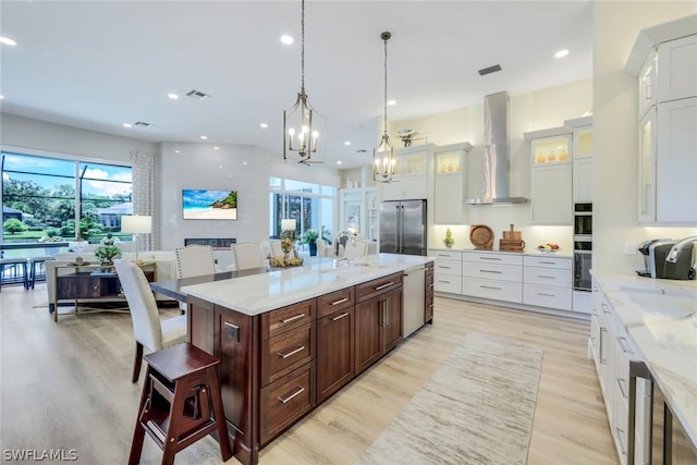 kitchen featuring stainless steel appliances, a large island with sink, sink, wall chimney exhaust hood, and a breakfast bar area