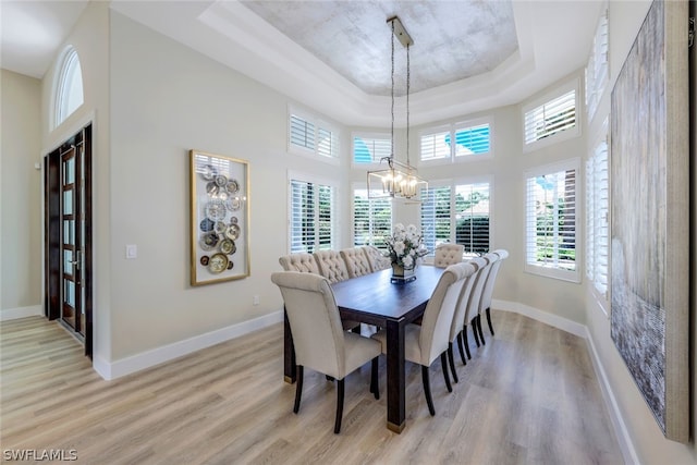 dining area featuring light wood-type flooring, a chandelier, a high ceiling, and a tray ceiling