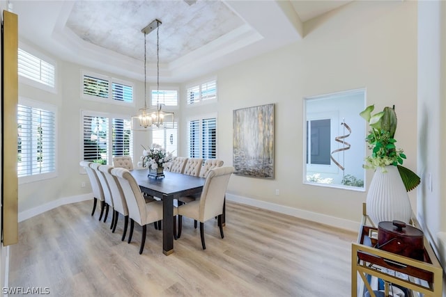 dining area featuring light wood-type flooring, a healthy amount of sunlight, and a raised ceiling