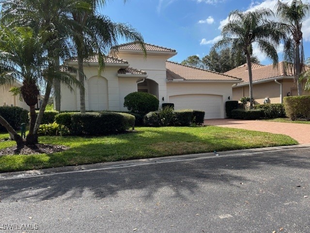 mediterranean / spanish house with a garage, a tiled roof, decorative driveway, a front lawn, and stucco siding