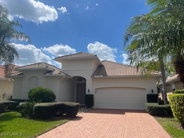 mediterranean / spanish house with decorative driveway, a tiled roof, an attached garage, and stucco siding