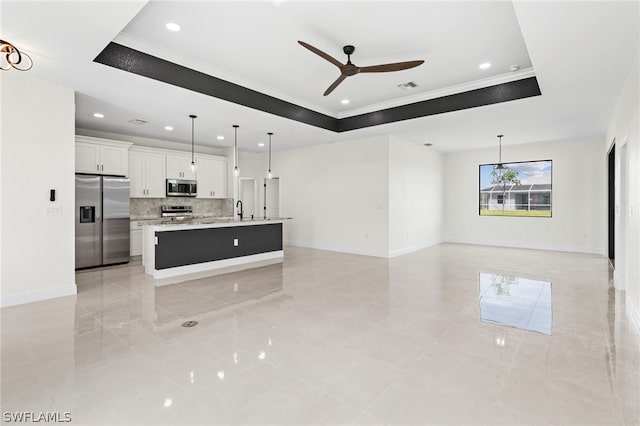 kitchen featuring a tray ceiling, white cabinetry, appliances with stainless steel finishes, and a center island with sink