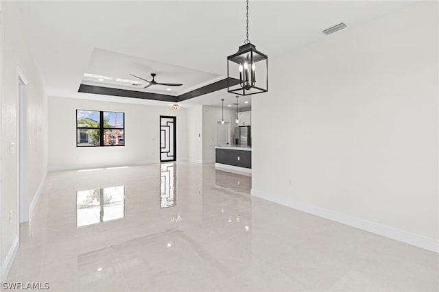 unfurnished living room with ceiling fan with notable chandelier and a raised ceiling