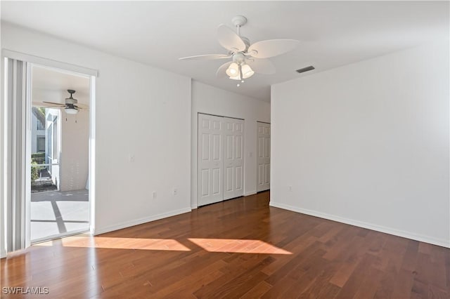 unfurnished bedroom featuring access to exterior, dark wood-type flooring, ceiling fan, and multiple closets