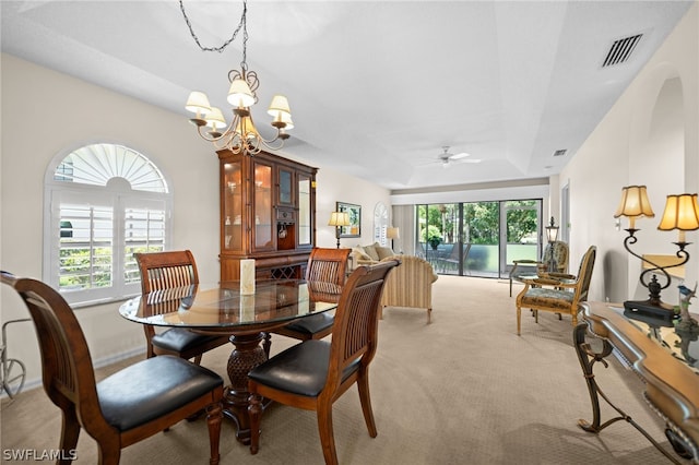 carpeted dining room with ceiling fan with notable chandelier and a tray ceiling