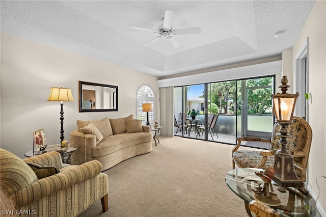 living room with ceiling fan, a textured ceiling, a tray ceiling, and carpet