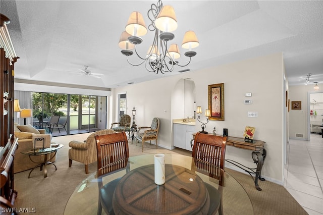 dining room with a textured ceiling, ceiling fan with notable chandelier, light tile patterned flooring, and a raised ceiling