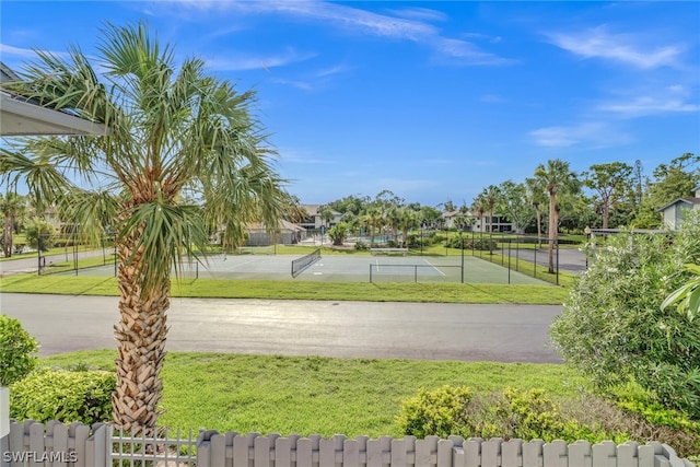 view of community featuring fence, a tennis court, and a lawn