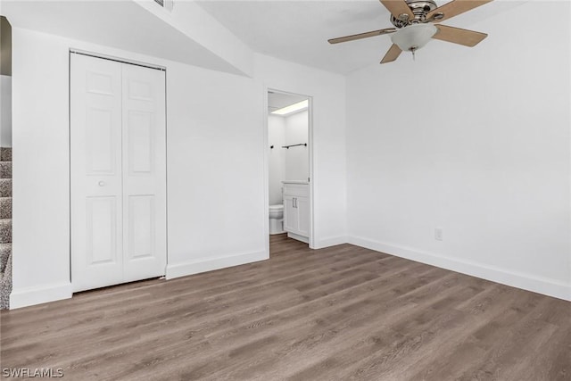 unfurnished bedroom with a ceiling fan, wood finished floors, baseboards, a closet, and connected bathroom