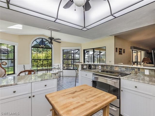 kitchen with light stone countertops, white cabinets, stainless steel range with electric stovetop, and ceiling fan