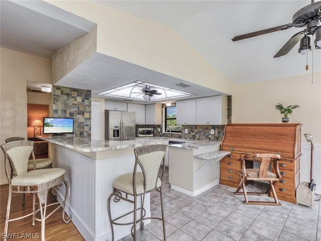 kitchen featuring kitchen peninsula, a kitchen bar, light stone counters, white cabinets, and stainless steel fridge with ice dispenser