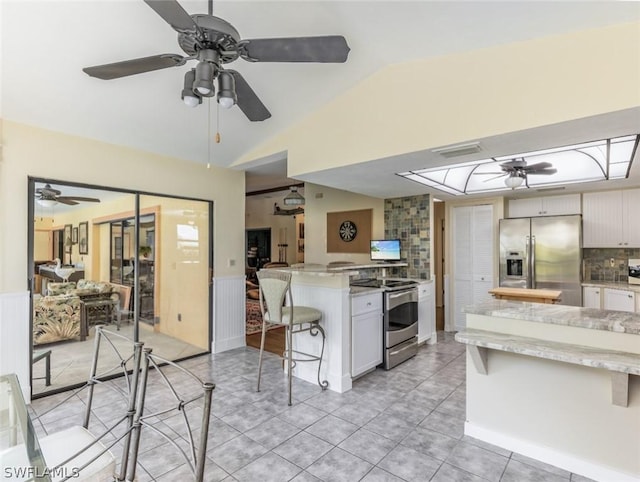 kitchen with white cabinets, a kitchen breakfast bar, vaulted ceiling, tasteful backsplash, and stainless steel appliances