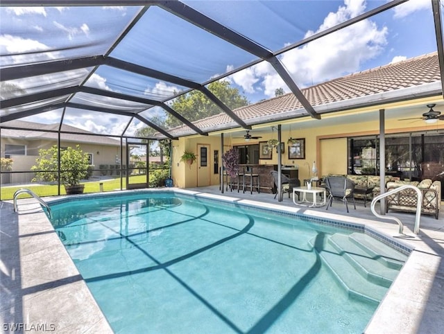 view of swimming pool featuring glass enclosure, ceiling fan, a patio area, and an outdoor bar