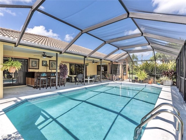 view of pool with a bar, a patio, ceiling fan, and a lanai