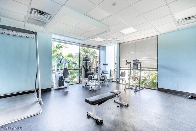 workout area with baseboards, visible vents, floor to ceiling windows, and a drop ceiling