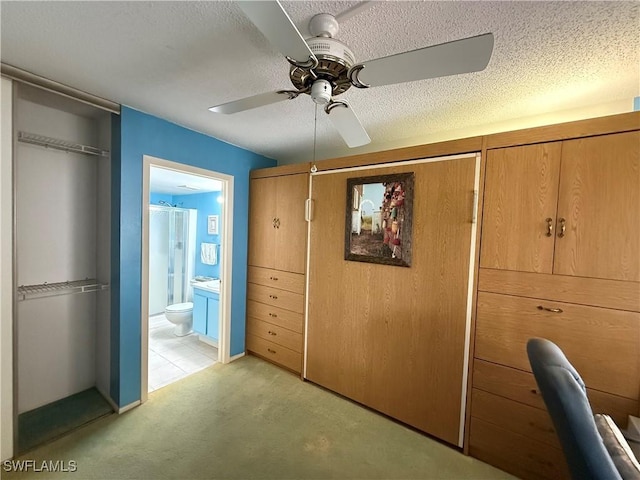 unfurnished bedroom featuring ensuite bathroom, a textured ceiling, ceiling fan, and light colored carpet