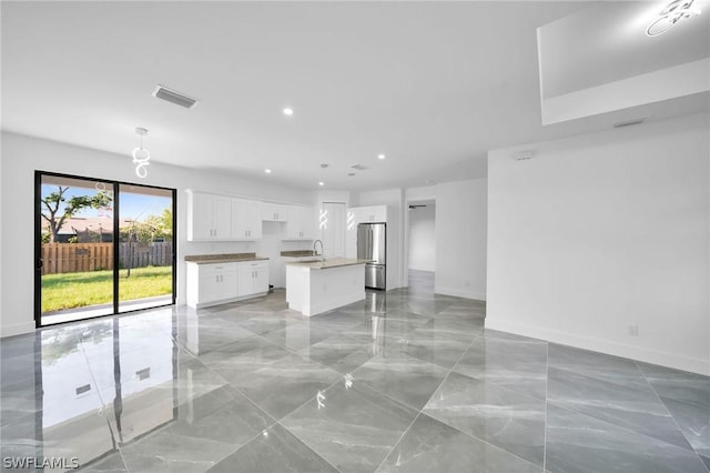 kitchen featuring sink, a kitchen island with sink, stainless steel refrigerator, and white cabinetry