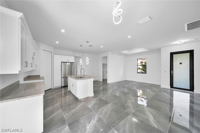 kitchen with decorative light fixtures, white cabinets, stainless steel refrigerator, and a center island with sink