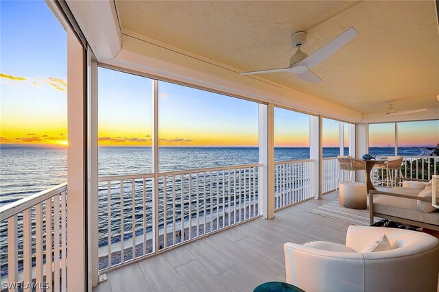 sunroom with ceiling fan, a beach view, and a water view