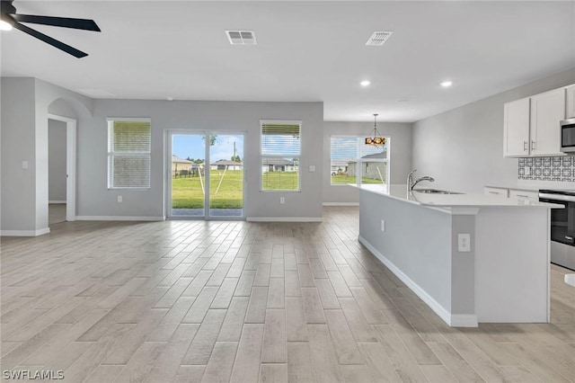 kitchen featuring sink, hanging light fixtures, a kitchen island with sink, white cabinets, and appliances with stainless steel finishes