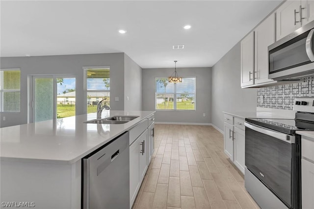 kitchen with stainless steel appliances, a kitchen island with sink, sink, a notable chandelier, and white cabinetry