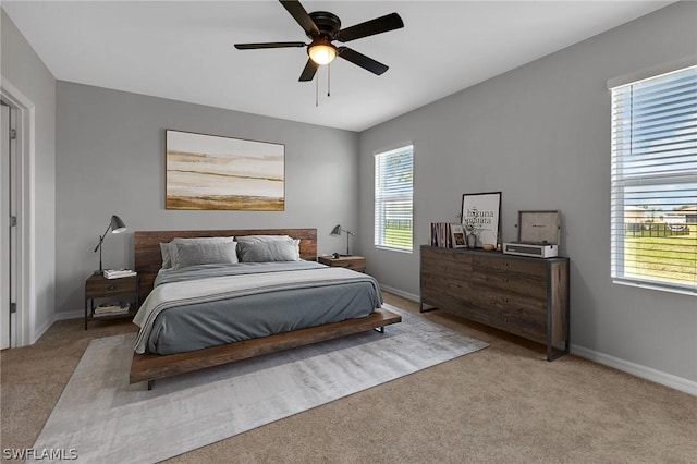 bedroom featuring ceiling fan, light carpet, and multiple windows