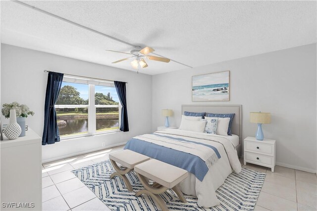 bedroom with light tile patterned floors, a textured ceiling, a water view, and ceiling fan