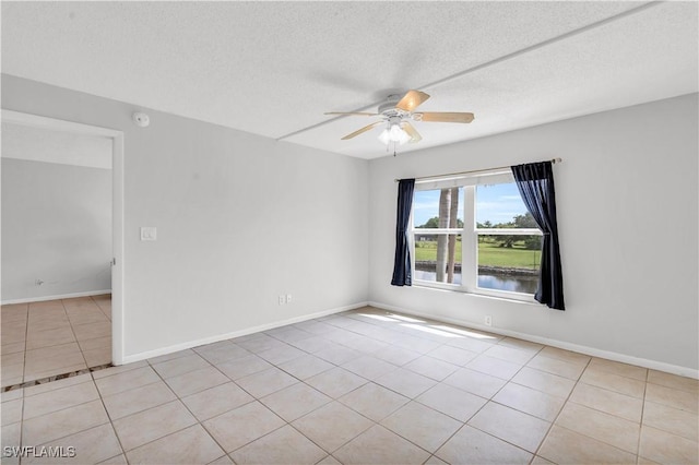 tiled empty room with ceiling fan, a water view, and a textured ceiling