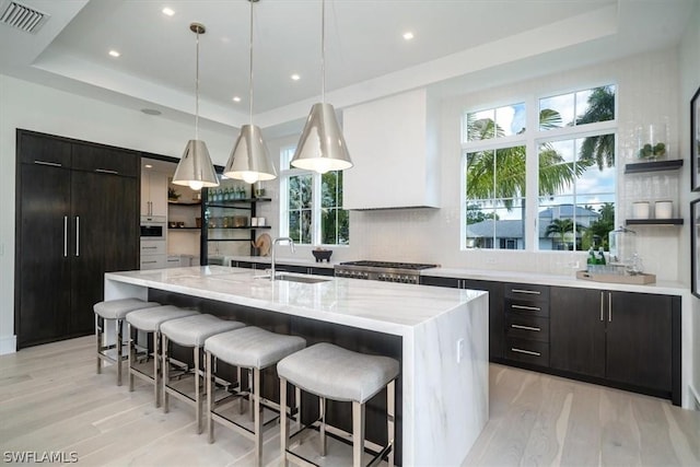 kitchen with decorative light fixtures, a tray ceiling, and an island with sink