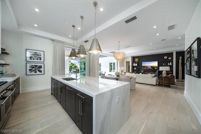 kitchen featuring a large island, sink, hanging light fixtures, a raised ceiling, and light wood-type flooring