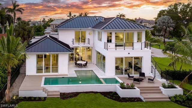 back house at dusk featuring a balcony, a fenced in pool, and a patio