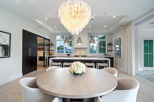 dining space featuring a tray ceiling, sink, light hardwood / wood-style floors, and an inviting chandelier