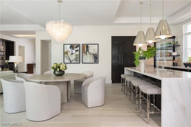 dining space featuring sink, a raised ceiling, light hardwood / wood-style flooring, and an inviting chandelier