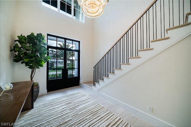 entryway with french doors, a towering ceiling, a chandelier, and tile patterned flooring