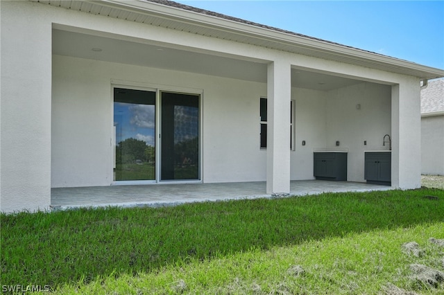 rear view of property featuring sink, a patio, and a lawn