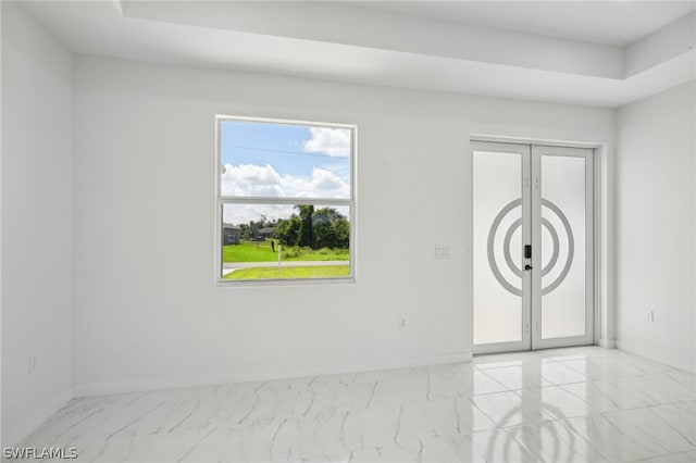 empty room featuring a raised ceiling, a healthy amount of sunlight, and light tile patterned floors