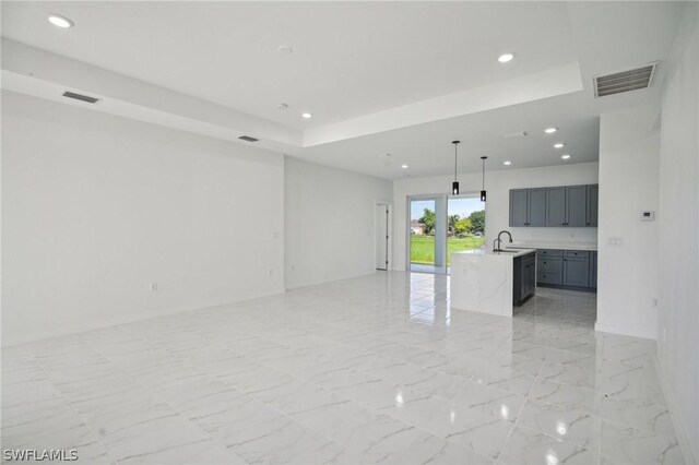 unfurnished living room featuring sink, light tile patterned flooring, and a raised ceiling