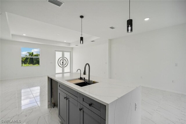 kitchen featuring sink, a tray ceiling, hanging light fixtures, and a center island with sink