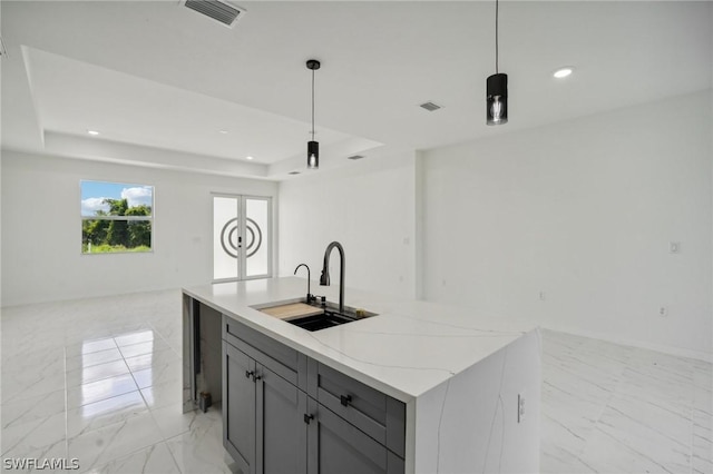 kitchen with pendant lighting, sink, a tray ceiling, and a kitchen island with sink